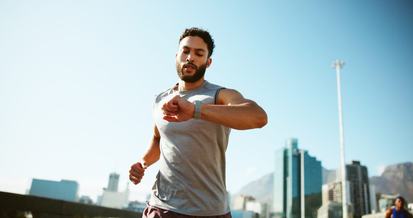 Book Combinations of Tests 2 A man checks his watch while running in an urban setting on a sunny day.